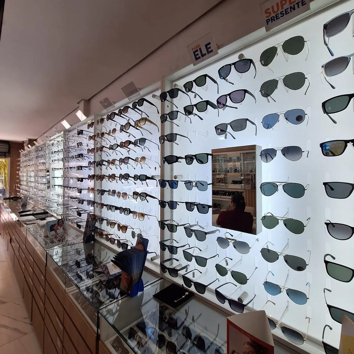 Ampla seleção de óculos de sol e de grau expostos na parede da VIP Joalheria e Ótica em Guaíba, incluindo modelos Ray-Ban e Oakley